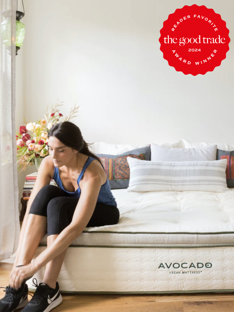 A model seated on an Avocado vegan mattress, putting on their shoes. The TGT 2024 Award Winner Badge is on the right corner of the image.