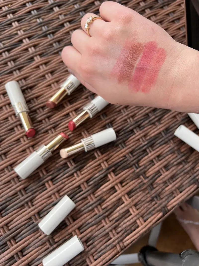 The back of a hand with swatches of four lipstick shades, with the lipsticks blurred in the background.