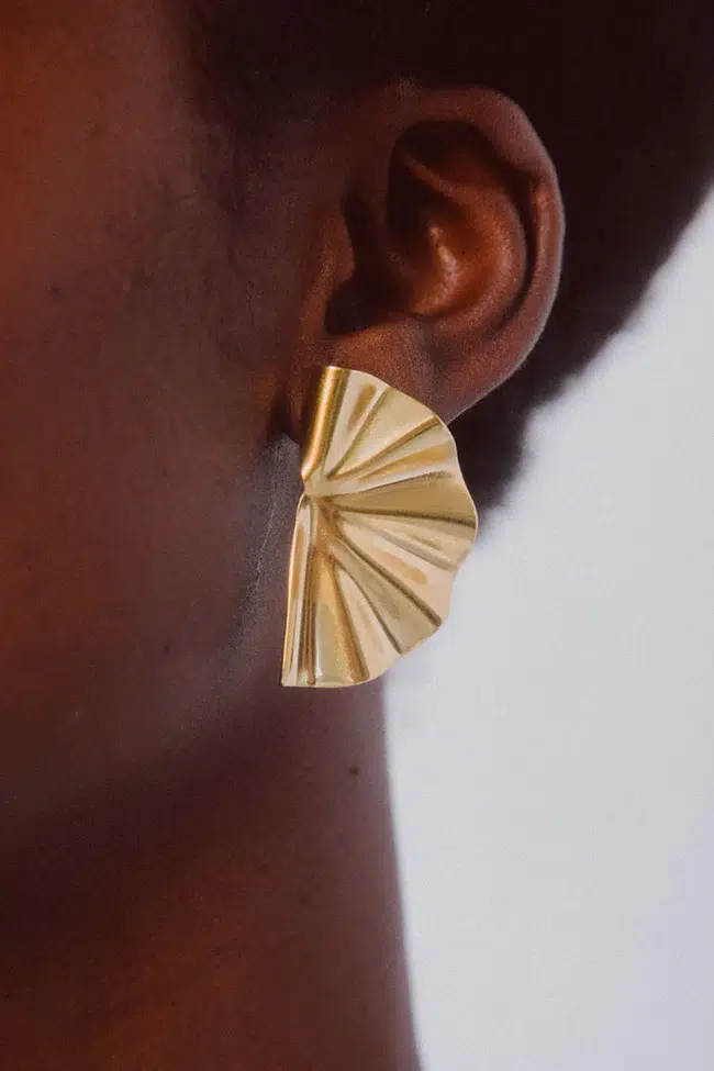 A side profile of a person wearing a large, gold, fan-shaped earring.