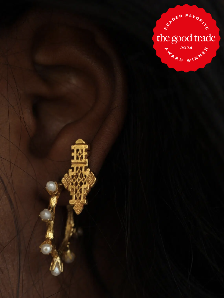 A close up shot of a model's ears wearing two earrings, one a gold hoop with pearls, and another large gold stud by Etsy shop Omi Woods. The TGT 2024 Award Winner Badge is on the right corner of the image. 