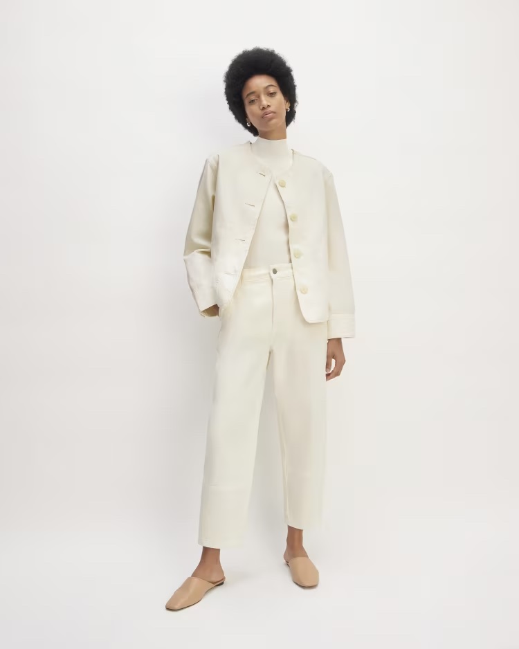 Woman modeling a cream-colored pantsuit with a double-breasted jacket and wide-leg trousers against a white background.