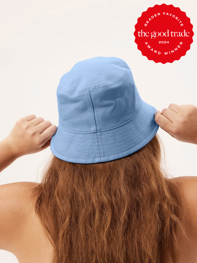 A woman models a sky blue bucket hat from Girlfriend Collective. The TGT 2024 Award Winner Badge is on the right corner of the image.