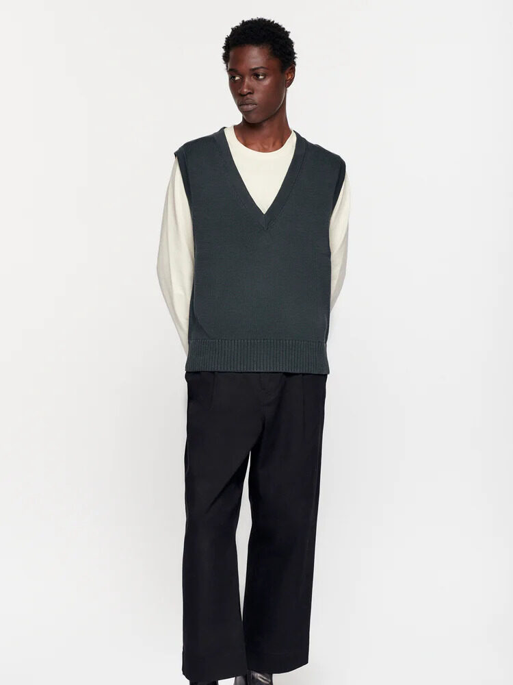 A model wearing a green knit vest with a white long sleeve under from Kotn.