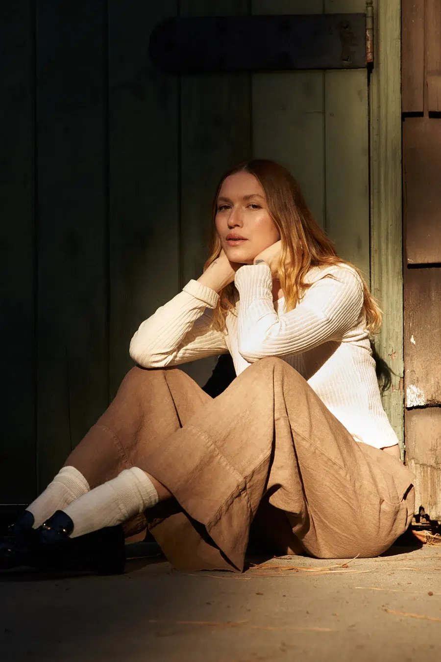 A woman sitting on the ground, leaning against a wall, bathed in sunlight.