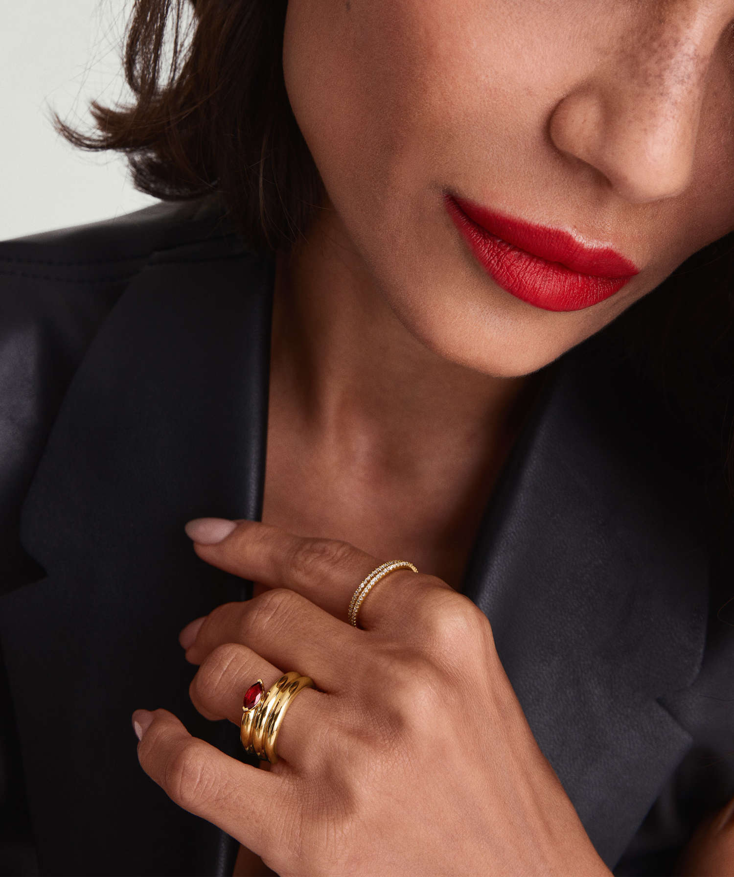 A close up shot of a model wearing red lipstick and a Mejuri Garnet Coil Ring in gold.