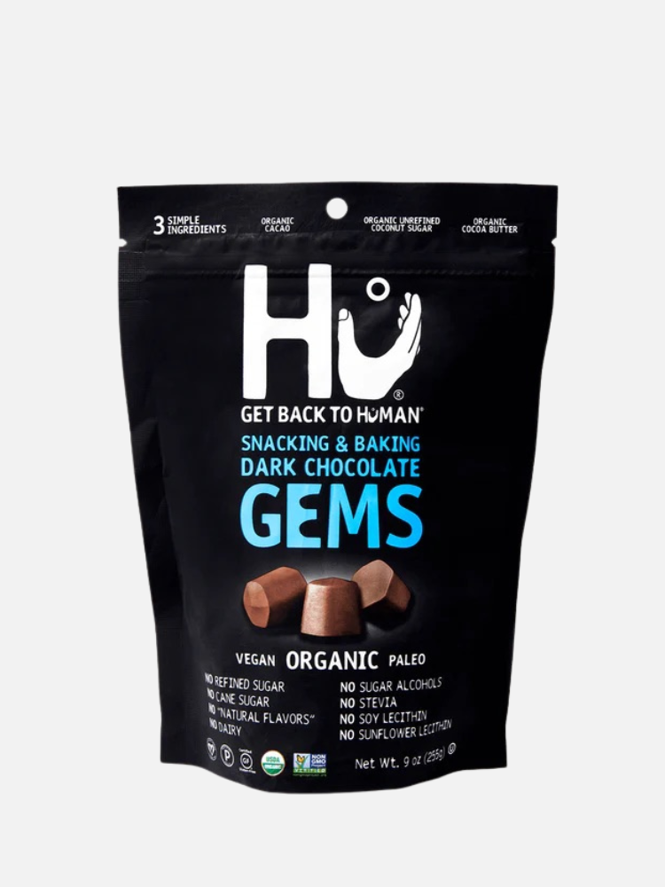 A sealed packet of hu-brand dark chocolate gems featuring "vegan," "no refined sugar," and "no sugar alcohols" labels on a sleek black background.