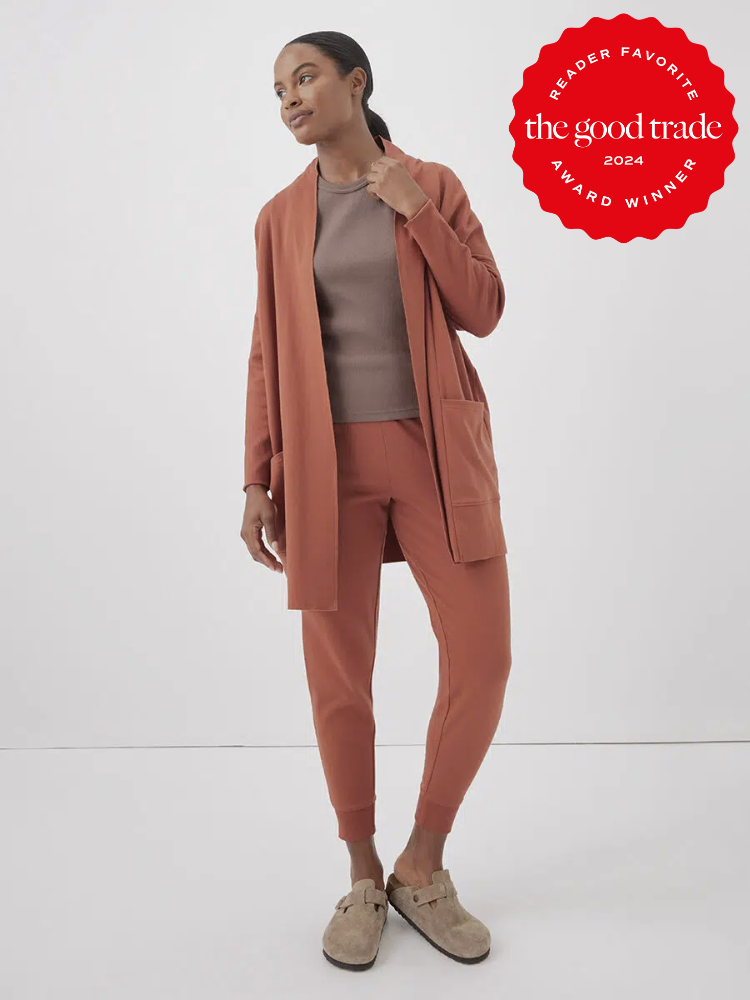A model wearing a burnt orange long cardigan with jumbo pockets from Pact. The TGT 2024 Award Winner Badge is on the right corner of the image.