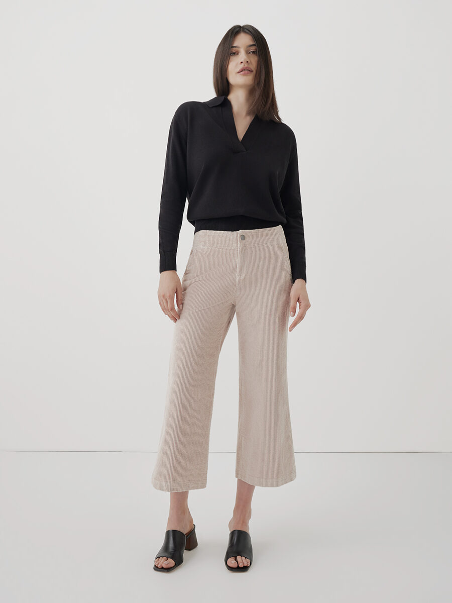 A model wearing a v-neck collared black sweater and ribbed corderoy wide leg pants from Pact.
