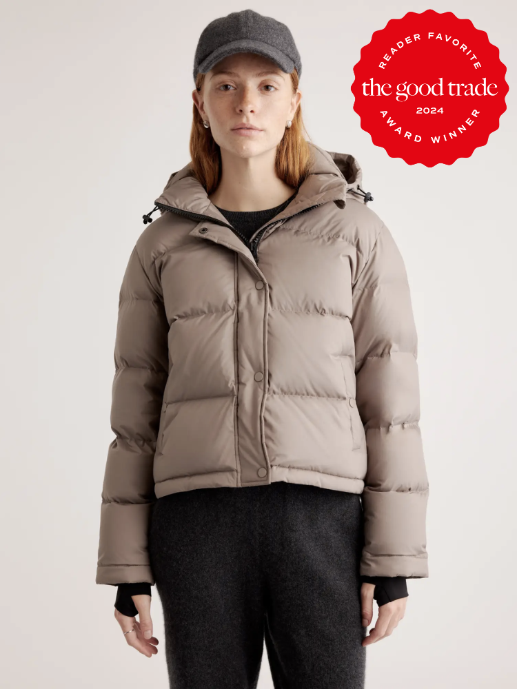 A model wearing a beige crop puffer jacket from Quince. A red Reader Favorite Award 2024 sticker by The Good Trade is on the top right hand corner.