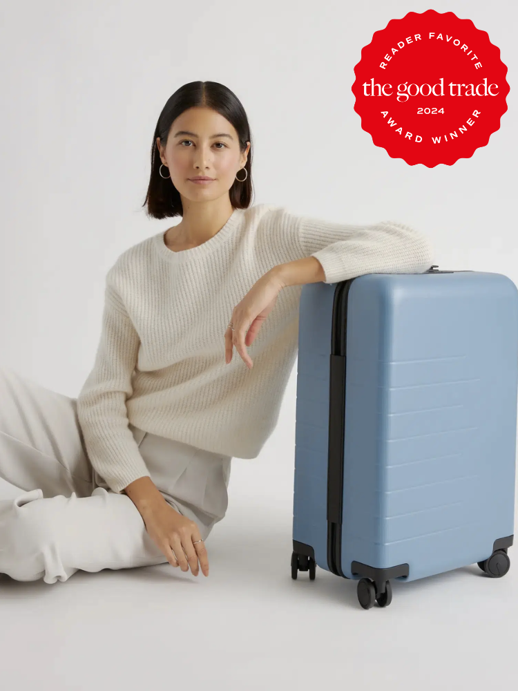 A model leans against a check-in blue suitcase from Quince. The TGT 2024 Award Winner Badge is on the right corner of the image.