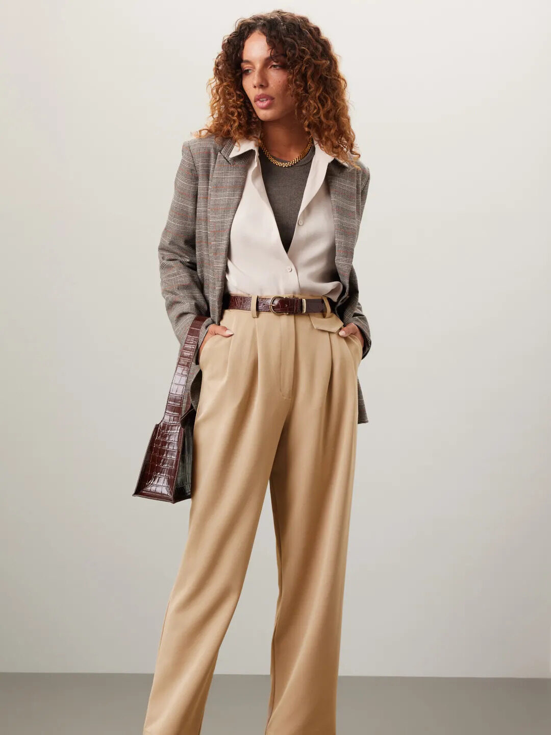 A model wearing a grey plaid blazer and beige dress pants from Rent the Runway. 