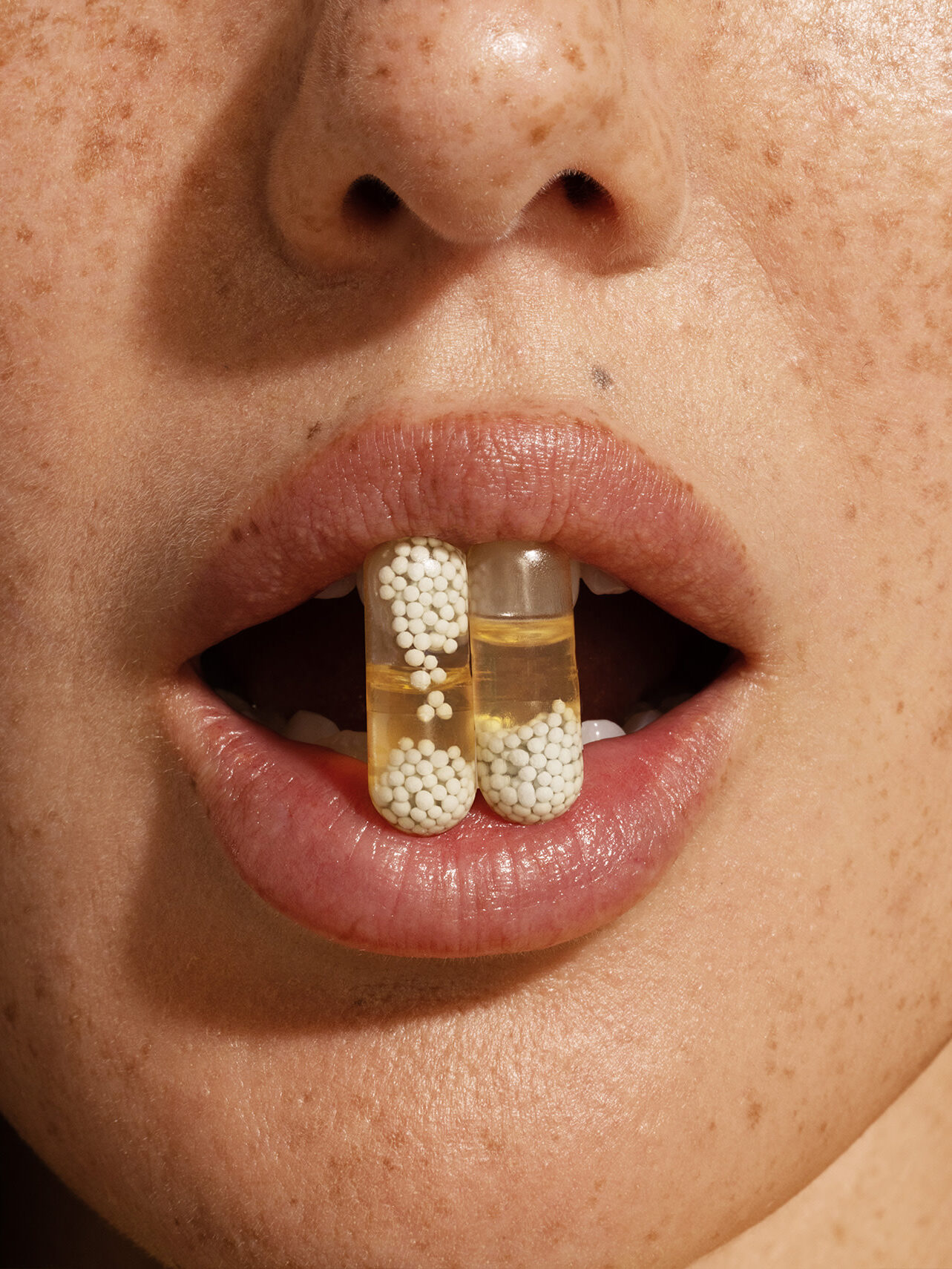 A close up of a model holding up two Ritual multivitamin capsules between their teeth. 