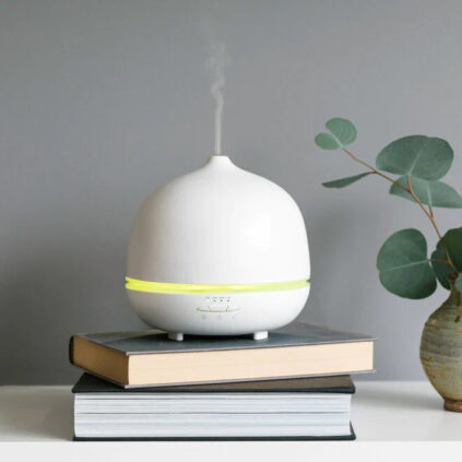 A white Saje diffuser set on a stack of books, humidifying the air.