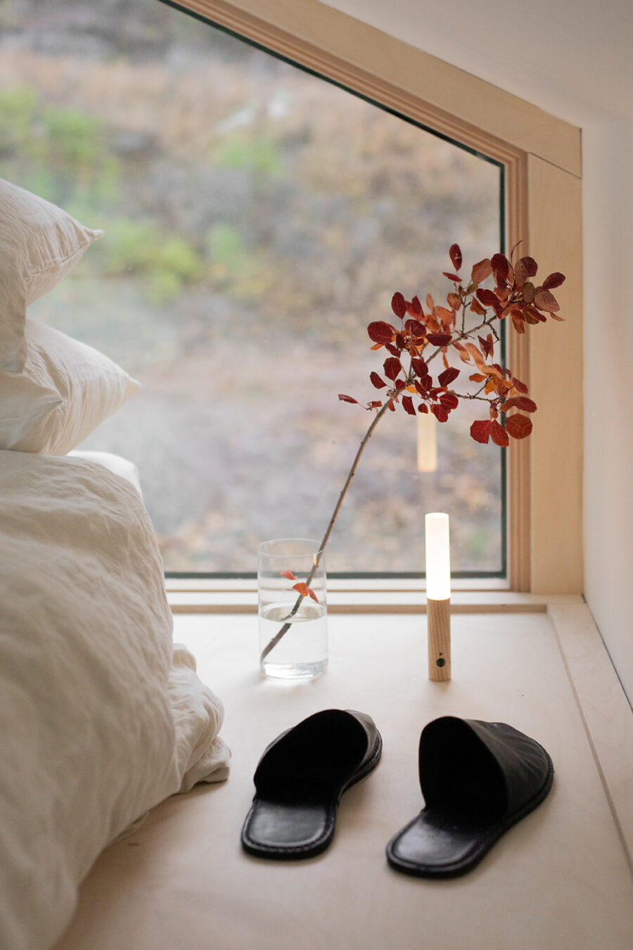 A pair of slippers next to a bed, with a window in front.