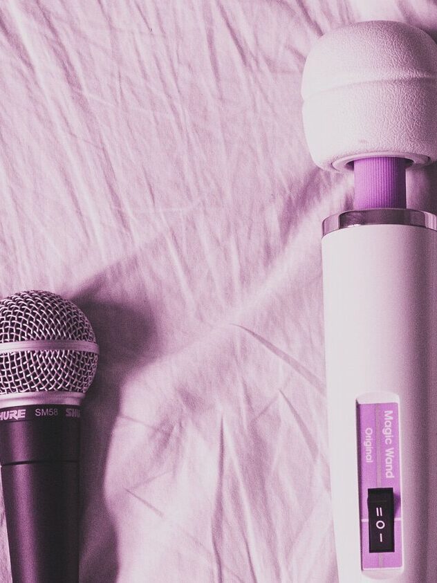 A photo of a mic and a vibrator on a bed, with a pink hue filter over the image.