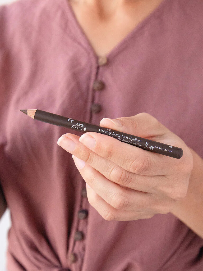 A close up of a model holding a 100% Pure eyeliner.