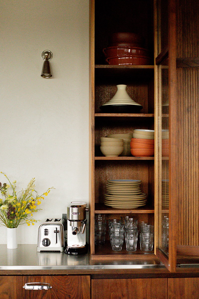 A kitchen cabinet stocked with dishes and a countertop with a toaster and coffee maker, next to a vase of yellow flowers.