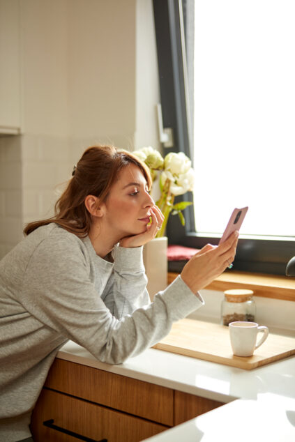 Portrait of a woman in a sweatshirt looking curiously at her mobile phone.