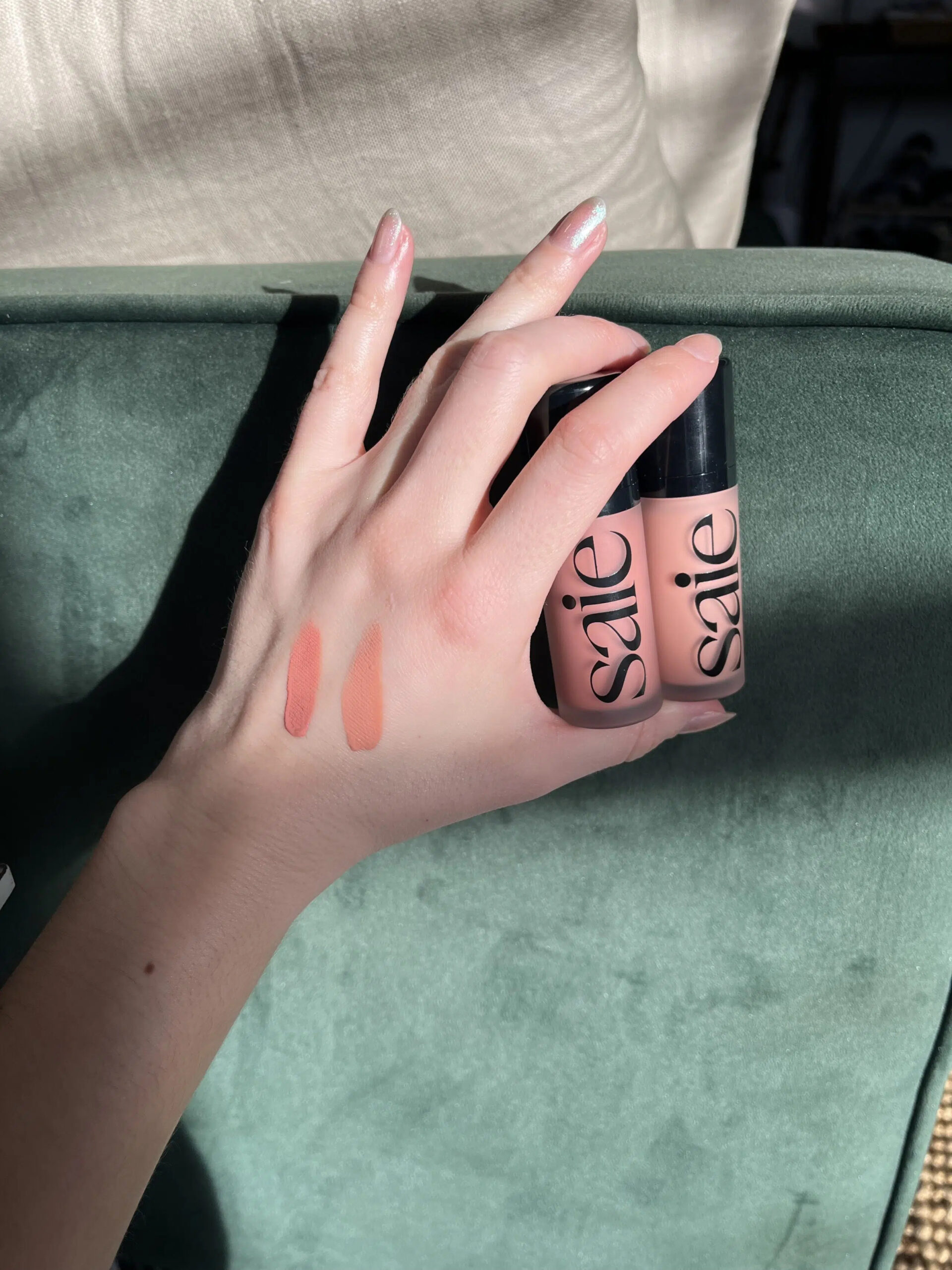 A TGT Editor holding up two bottles of Saie blush, with two swatches on their hand. 