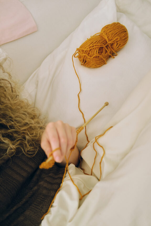 Young woman with knitting needles doing knit work with orange yarn.