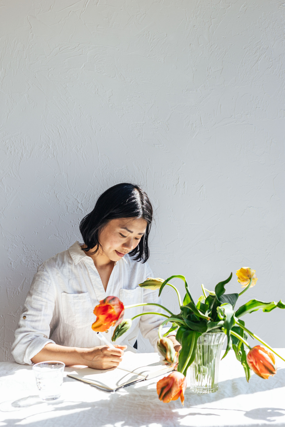 Asian woman sitting at a table with flowers and a notebook.