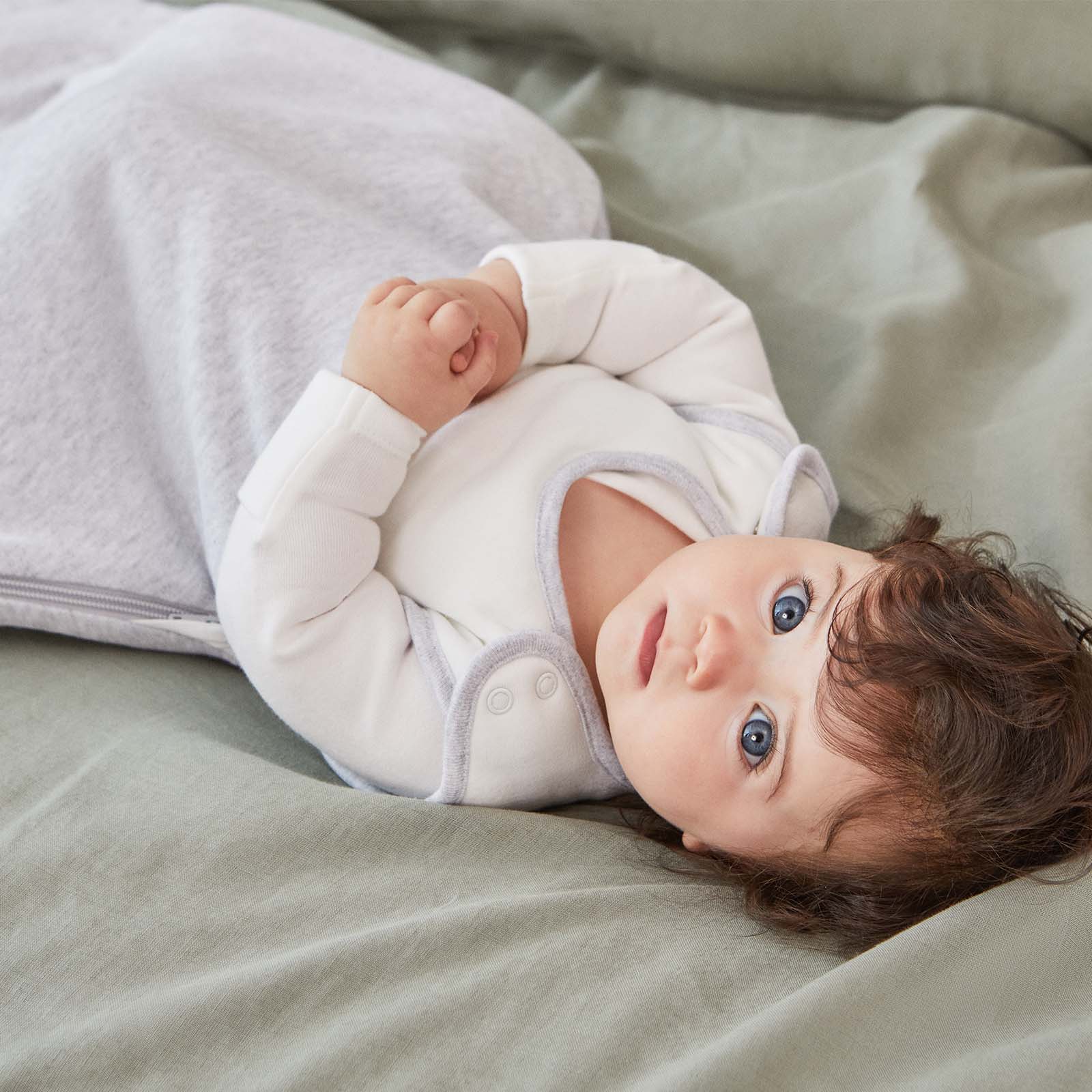 A blue-eyed baby laying in a white onesie on a green sheet.
