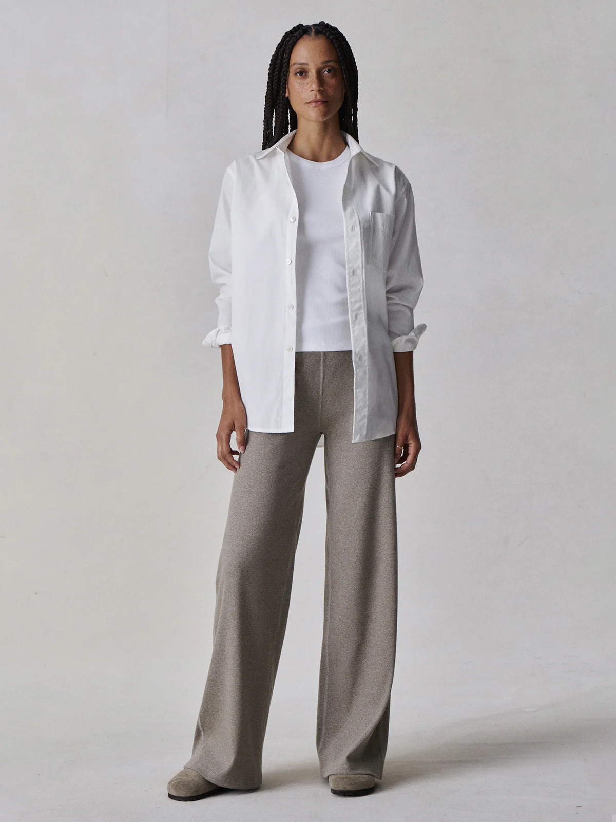 The model is wearing a white shirt and wide leg pants.