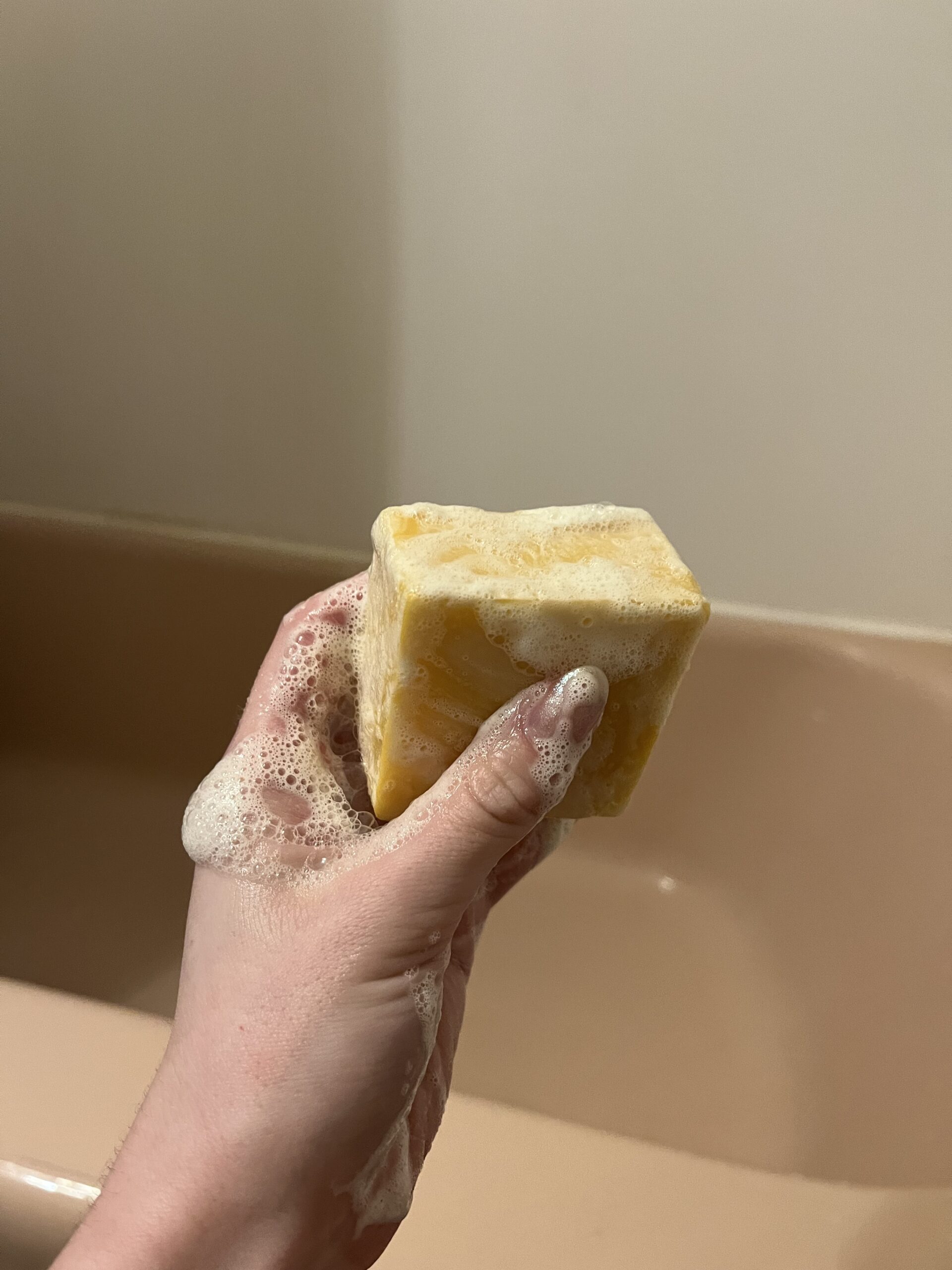 A person holding a sudsy yellow sponge in a bathtub.