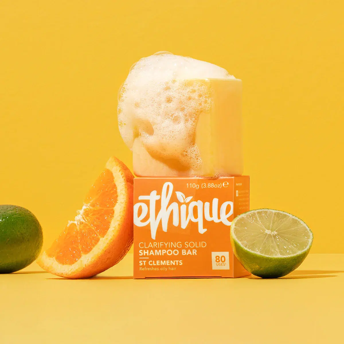 A shampoo bar with foam on top, set against a yellow background flanked by citrus fruit slices.