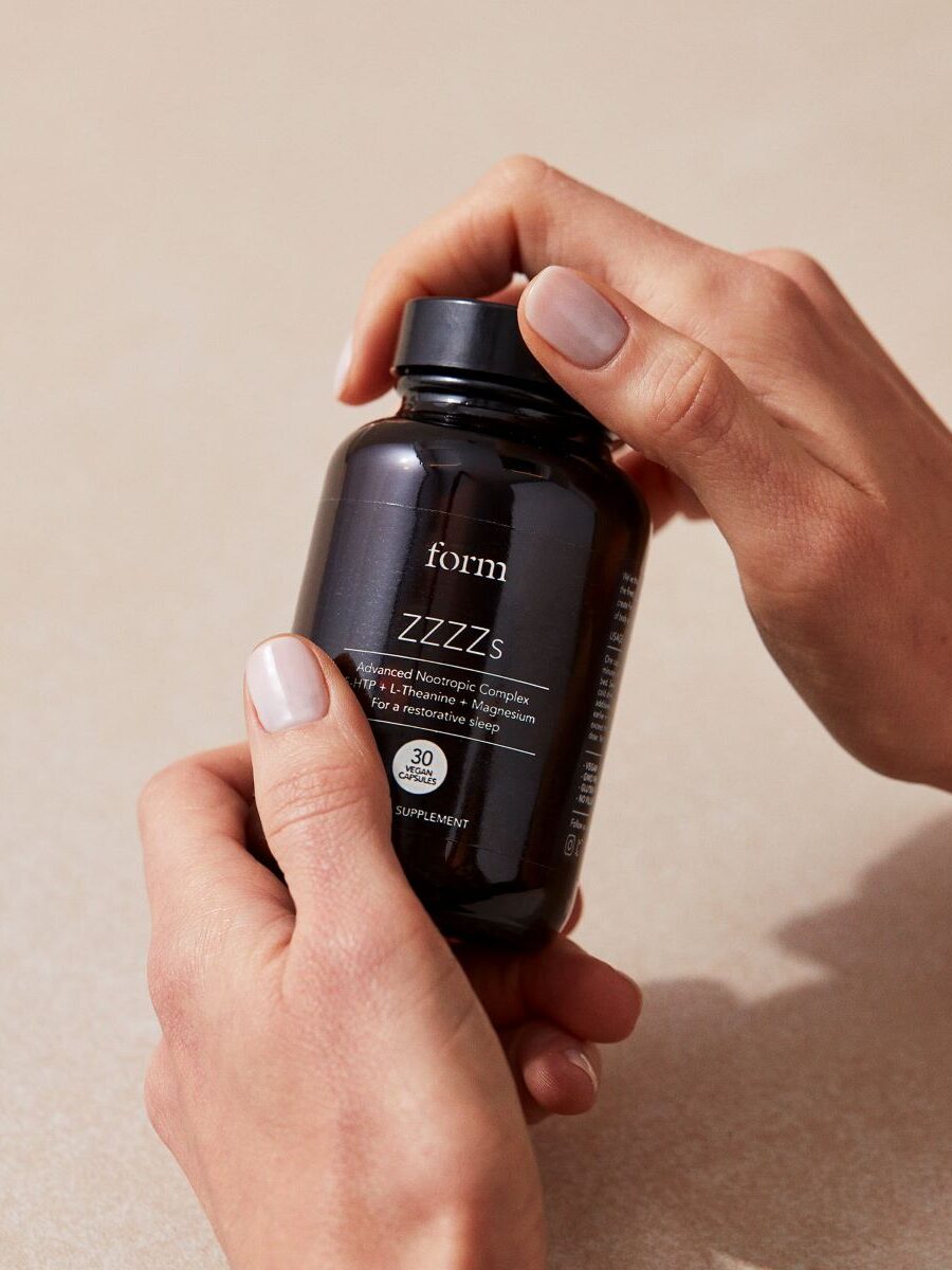 A pair of hands holding a glass jar of Form's ZZZ's nootropics complex.