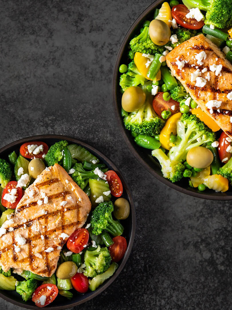 Two bowls of grilled salmon on veggies, made from a Fresh N Lean delivery box. 