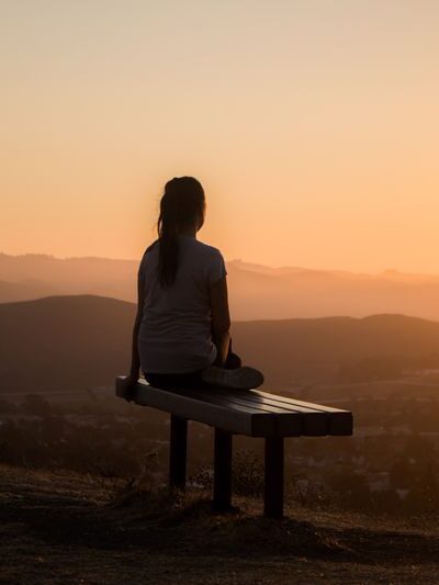 A woman sitting on a bench at sunset.