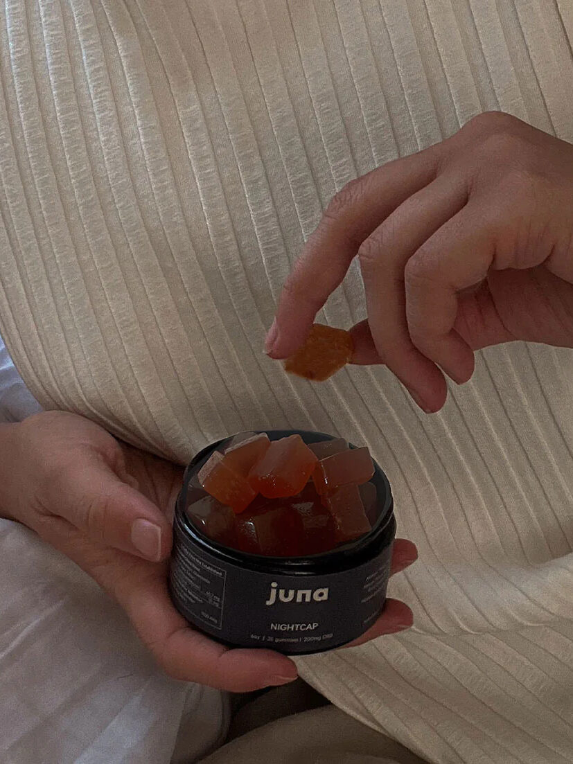 A close up shot a model holding an open jar of Juna Nightcap in one hand and taking a sleep supplement gummy out of the jar with the other hand. 