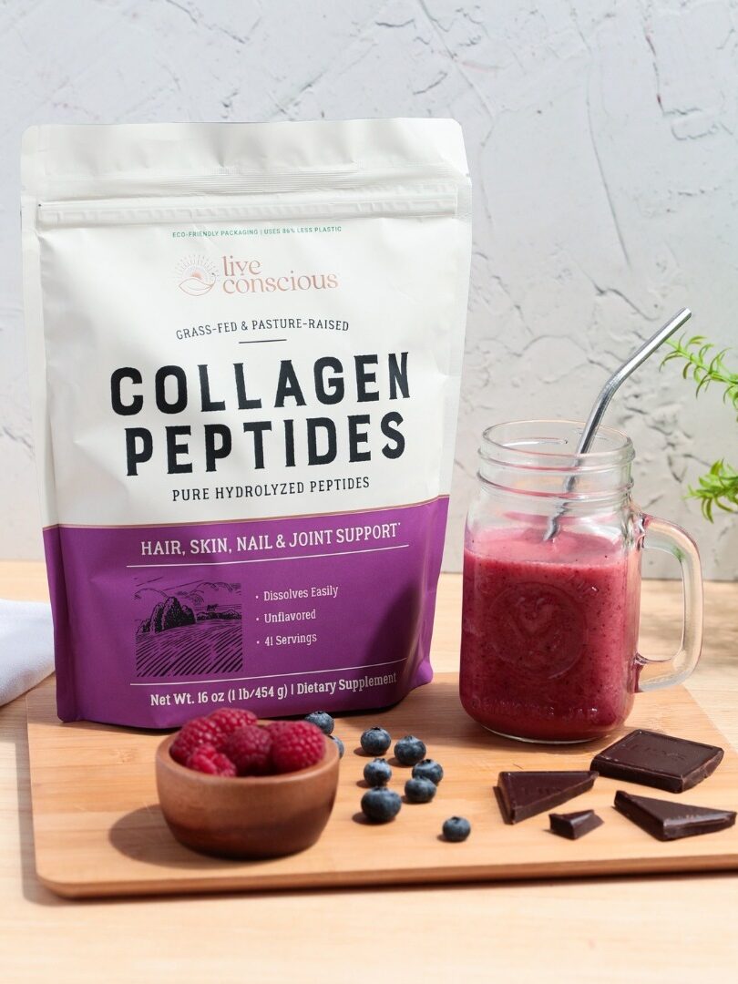 A packet of Live Consious collagen next to a bowl of berries, chocolate squares, and a berry smoothie. 