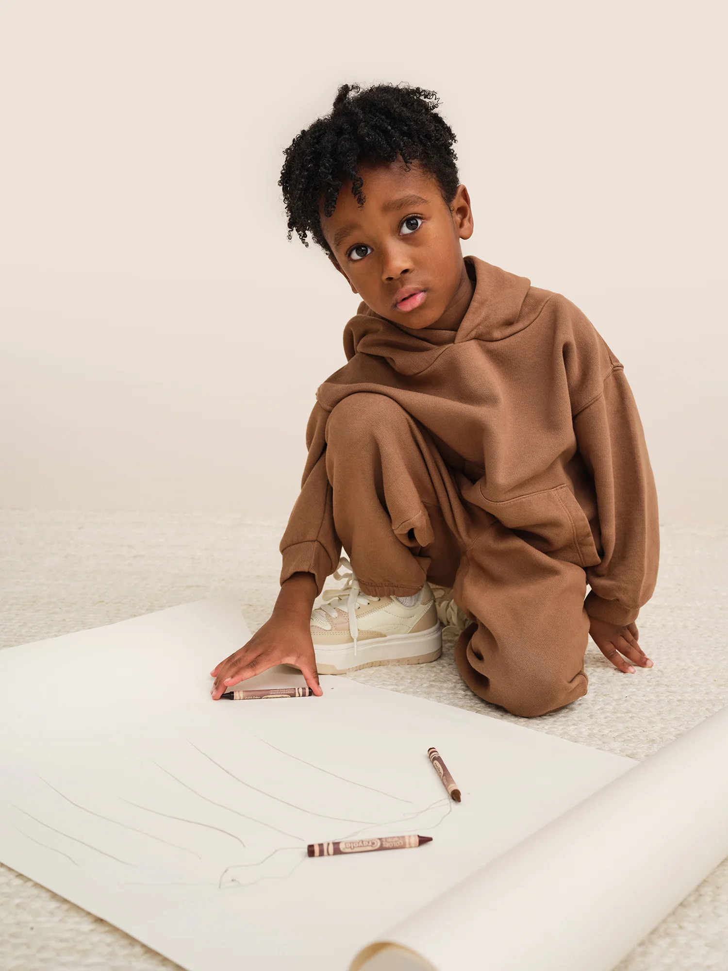 A young boy sitting on the floor and drawing on a piece of paper.