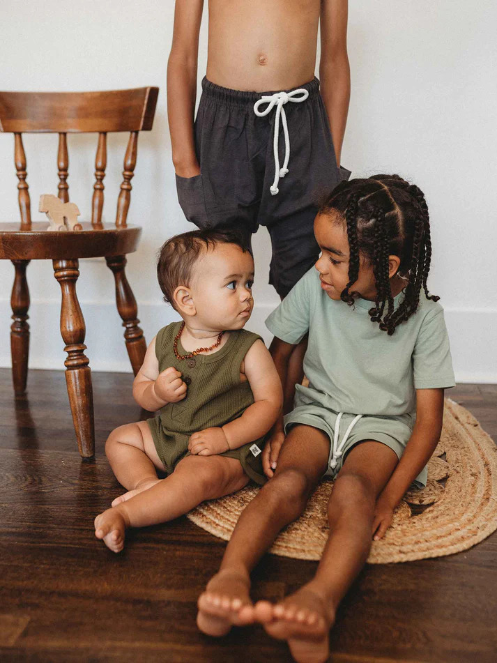 Three children sitting on a rug in front of a wooden floor.