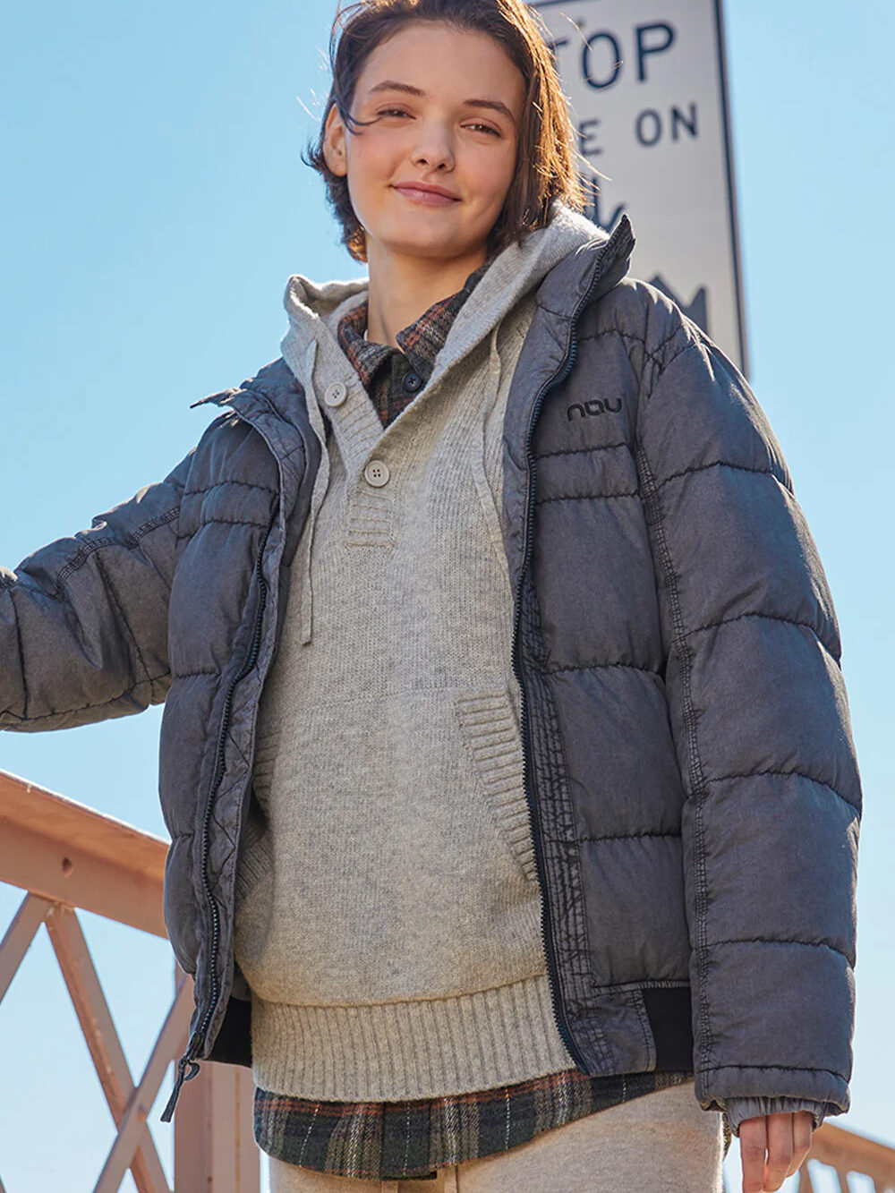 A woman is standing on a bridge wearing a grey puffer jacket.