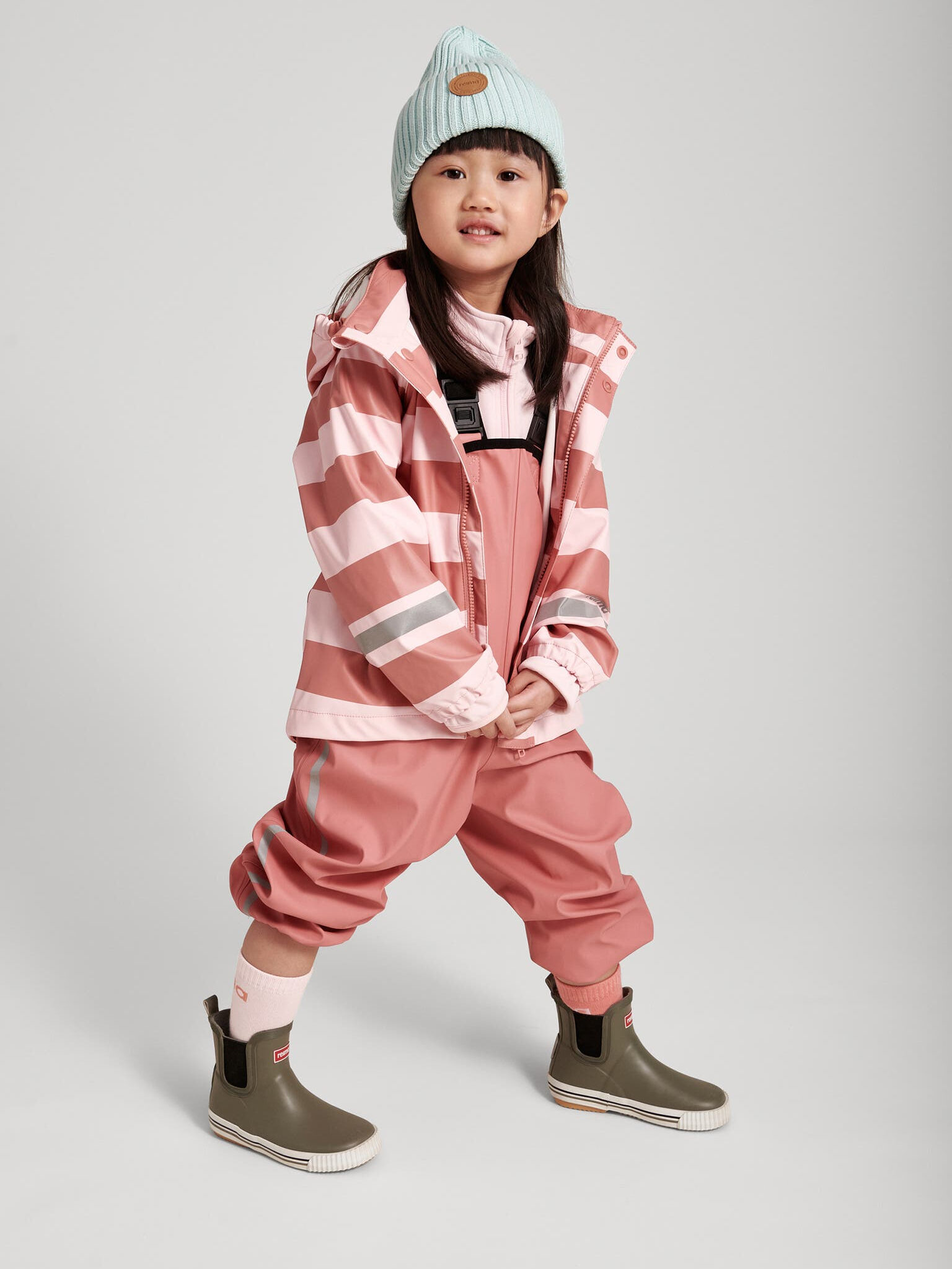 A little girl wearing a pink striped raincoat and hat.