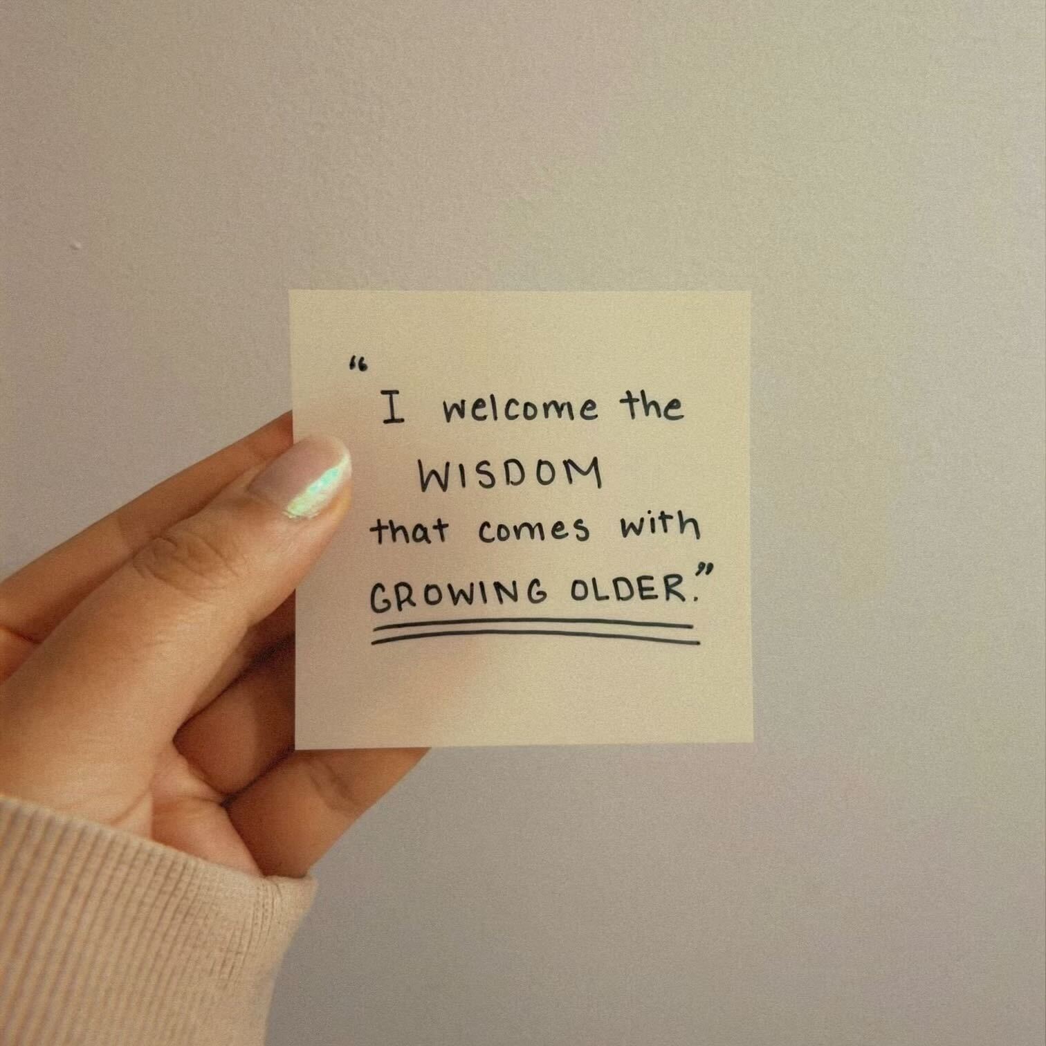 A sticky note held up, reading "I welcome the wisdom that comes with growing older". 