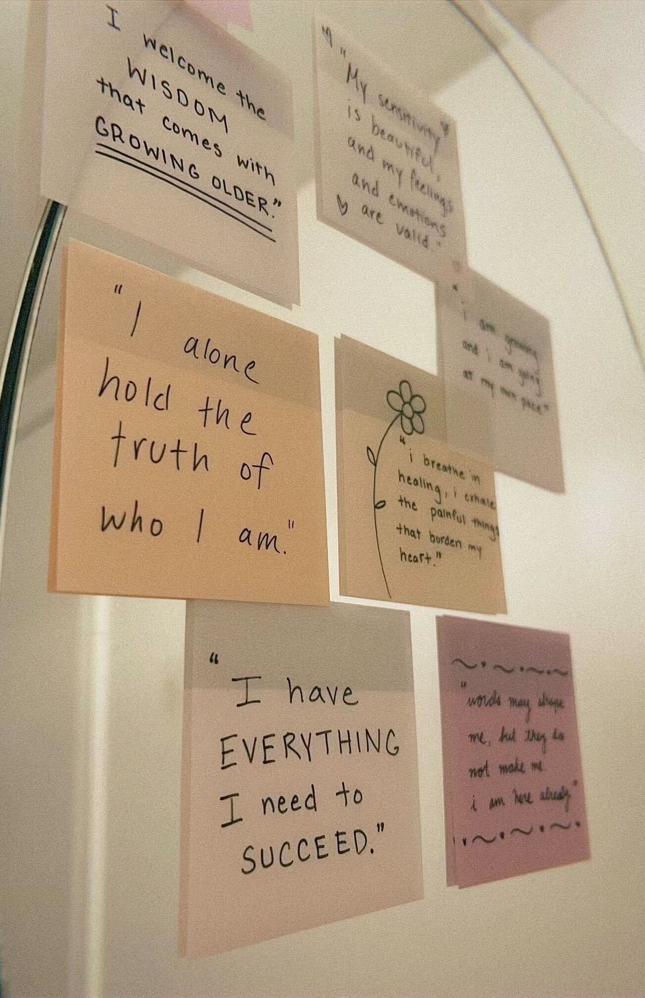Pastel transparent sticky notes with positive affirmations written on them, posted on a bathroom mirror.