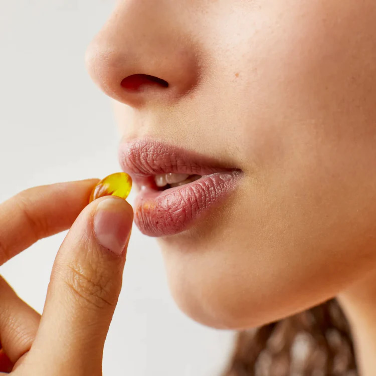 A woman is taking a Prima CBD capsule into her mouth.