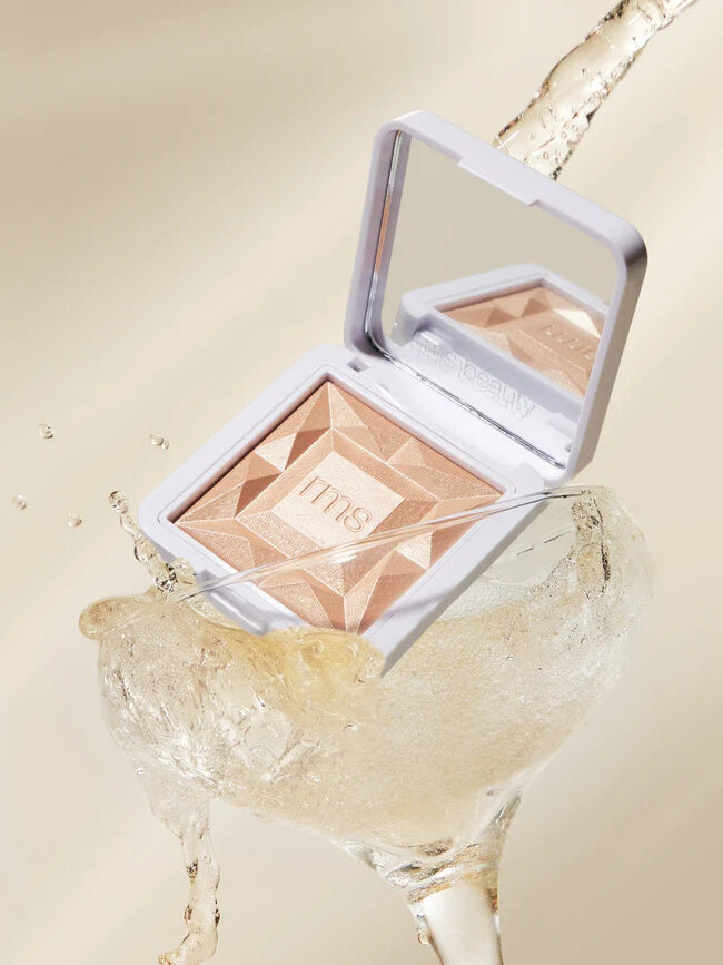 An RMS Beauty highlighter in a cocktail glass filled with liquid. 