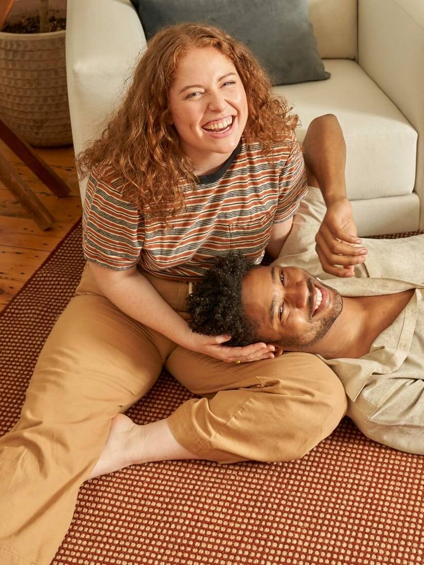 A couple laughing, laying on a Sabai Field rug.