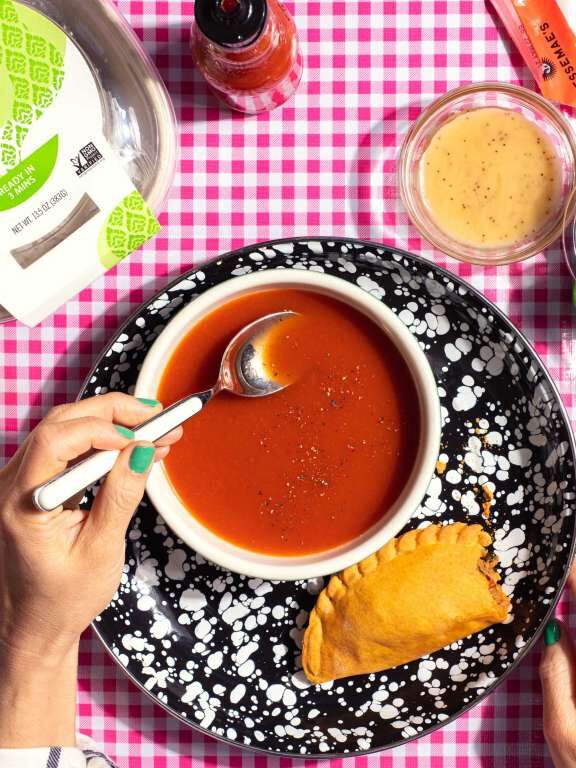 A bowl of tomato soup and an empanada on a red checkered tablecloth, made from Sunbasket's meal delivery kit.