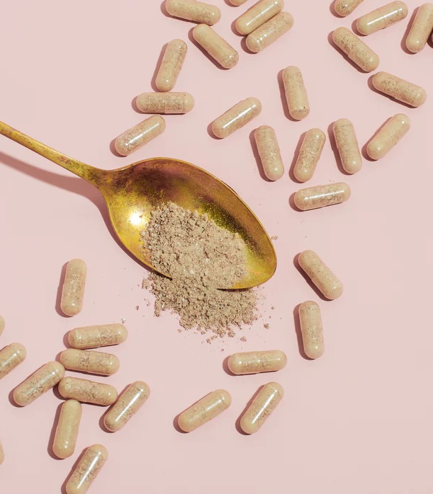 A spoon full of prenatal pills and powder on a pink background.