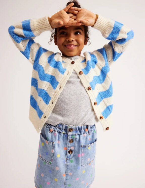 A little girl wearing a blue and white striped cardigan and polka dot skirt.