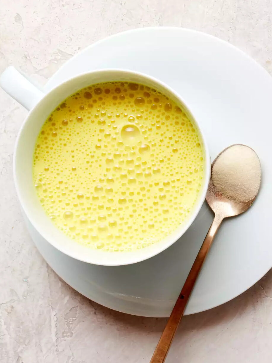 A close up of a turmeric latte with a spoon of Thrive Market collagen next to it. 