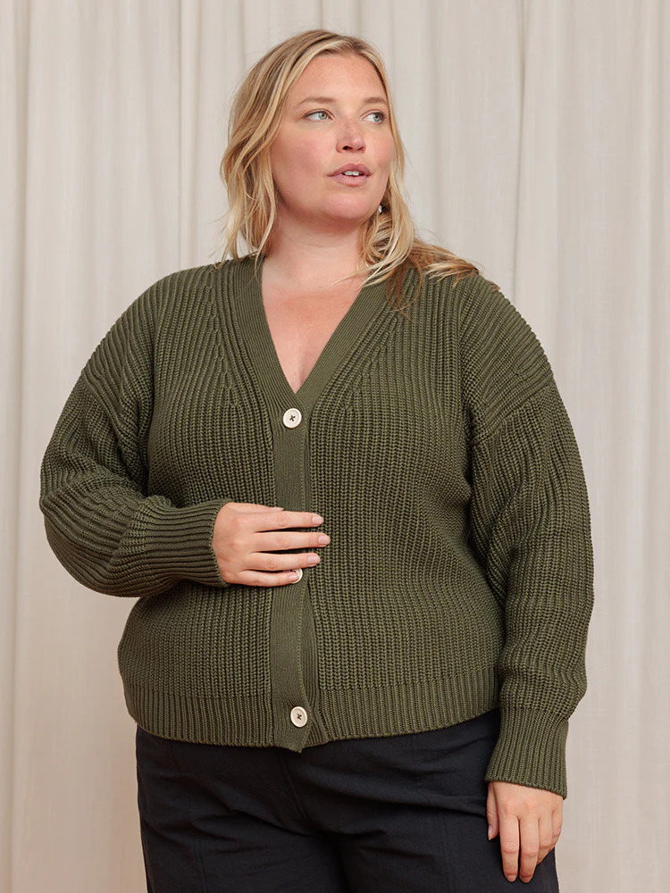 A woman wearing a green cardigan and black pants.