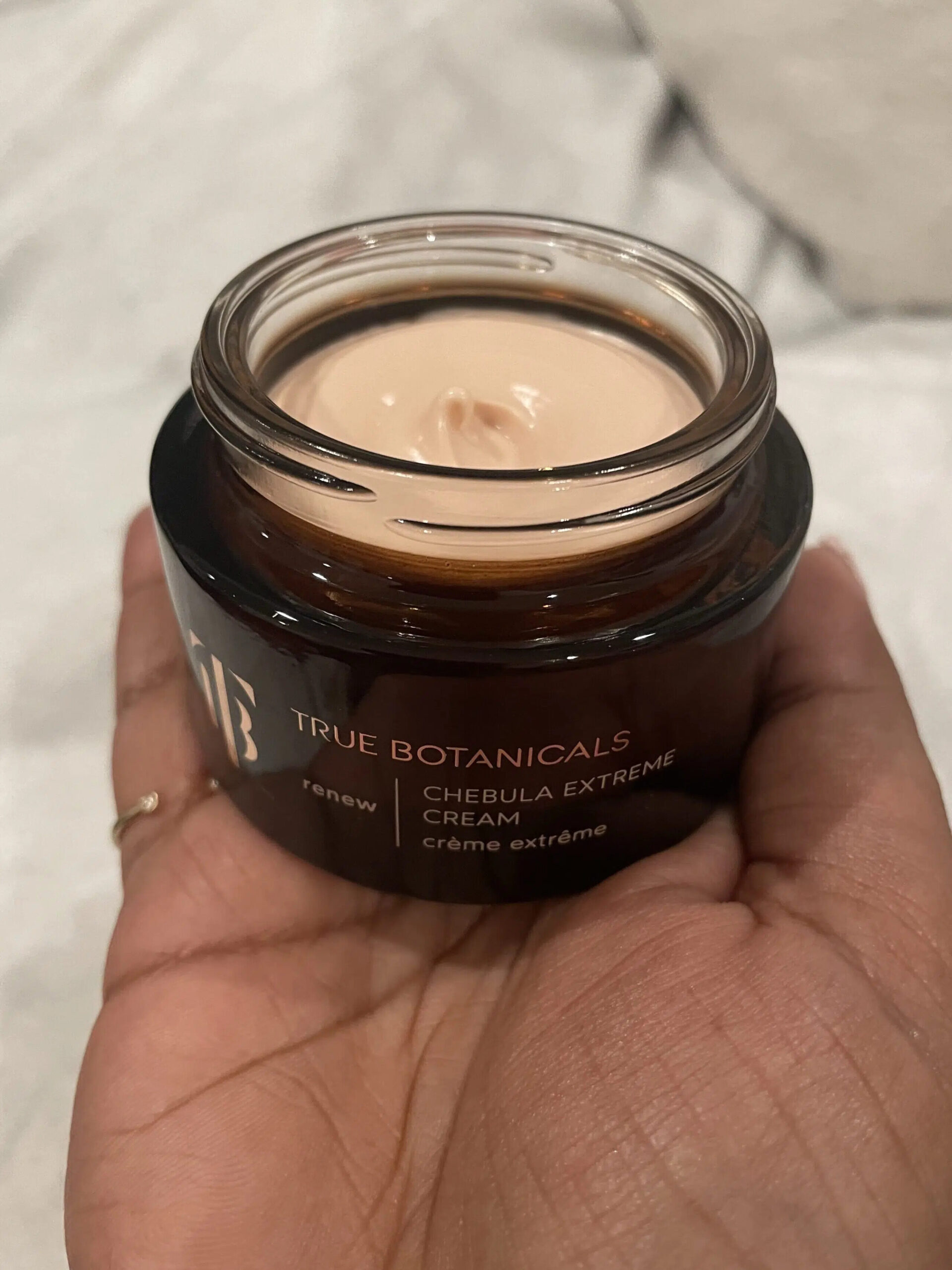 A TGT editor holding an open jar of True Botanicals Chebula Extreme Cream. 