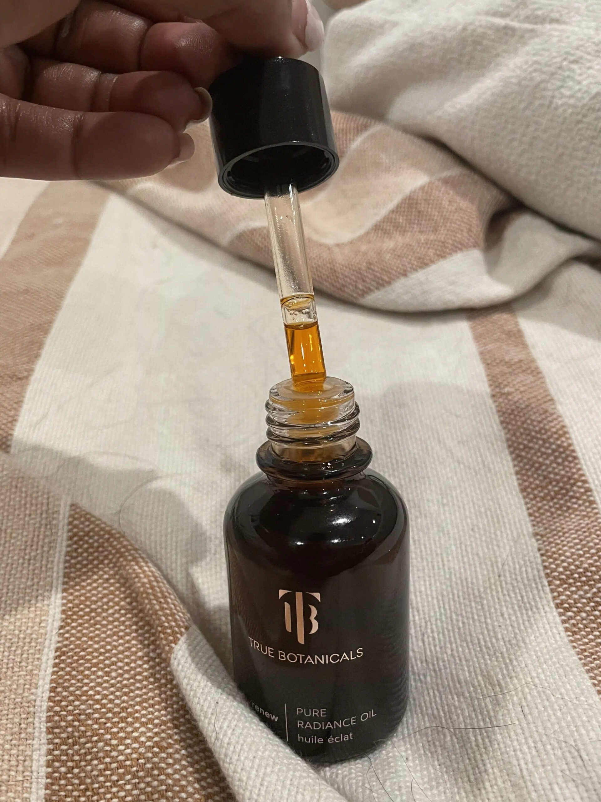 A TGT editor removing a dropper of oil from the True Botanical's Pure Radiance Oil bottle. 